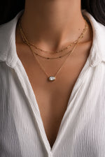 Gold east-west oval CZ pendant layered with two fine gold chains on a model.