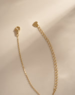 Close-up of the gold necklace's lobster clasp, extension chain and heart-shaped end tag.