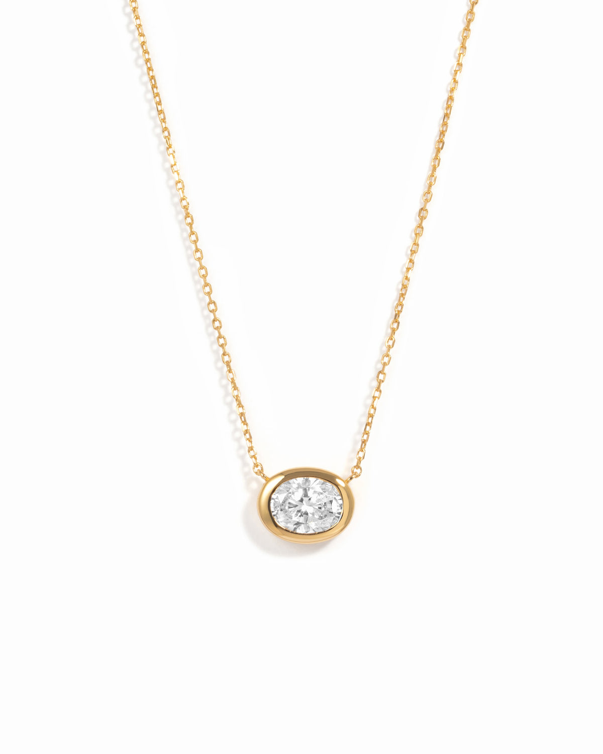 Gold east-west oval CZ bezel pendant necklace on a white background.