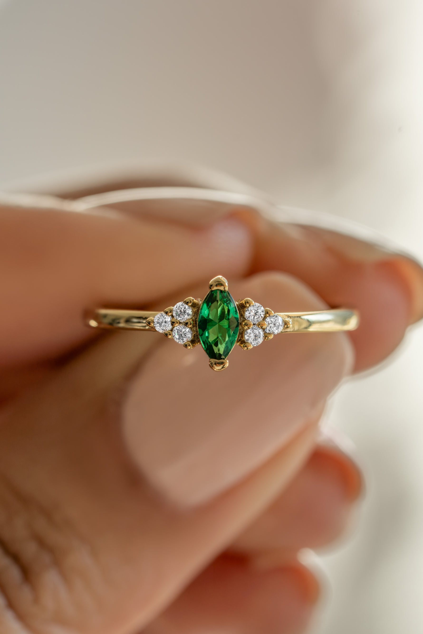 gold diamond emerald marquise ring held between fingers
