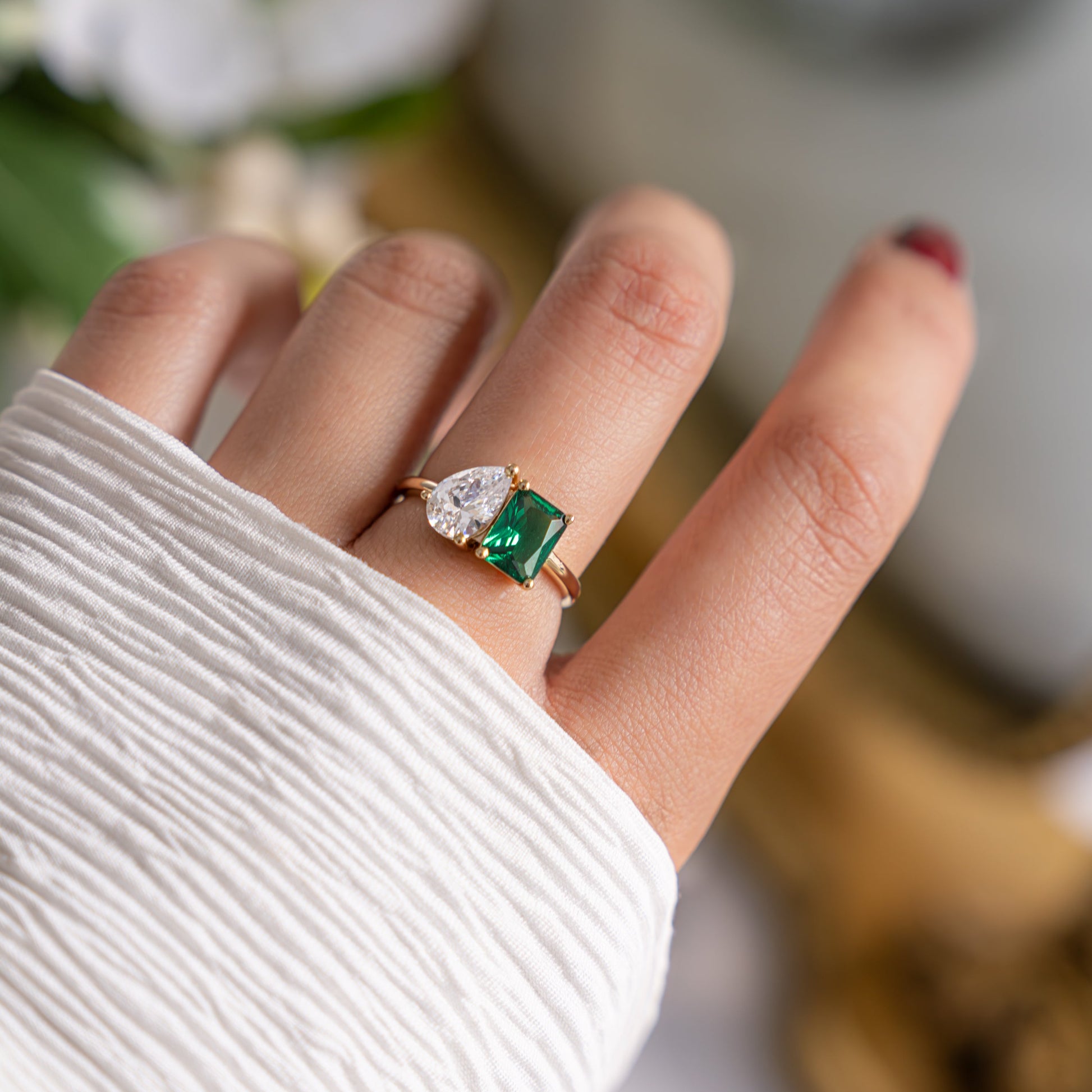 A close-up of a model's hand showcasing a stunning Toi et Moi Ring with an emerald cut and pear stone diamond.