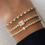 closeup image of model wearing tennis bracelet stack featuring a emerald green and white cubic zirconia bracelet, a emerald cut tennis bracelet, and a round bezel tennis bracelet