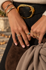 Gold fluted bangle and other gold bracelets worn with rings and a black swimsuit.