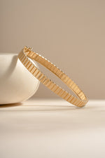 Gold fluted bangle shown upright at an angle against a cream background.