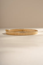 Gold fluted bangle resting on a cream background.