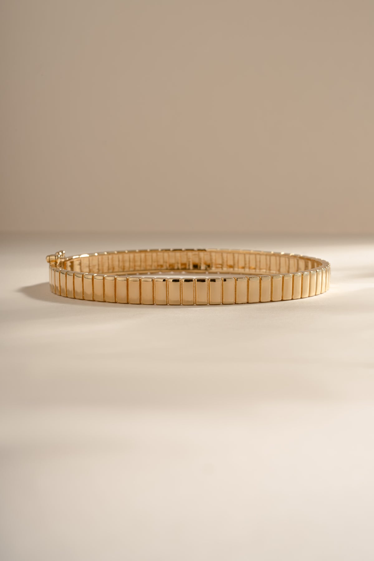 Gold fluted bangle resting on a cream background.