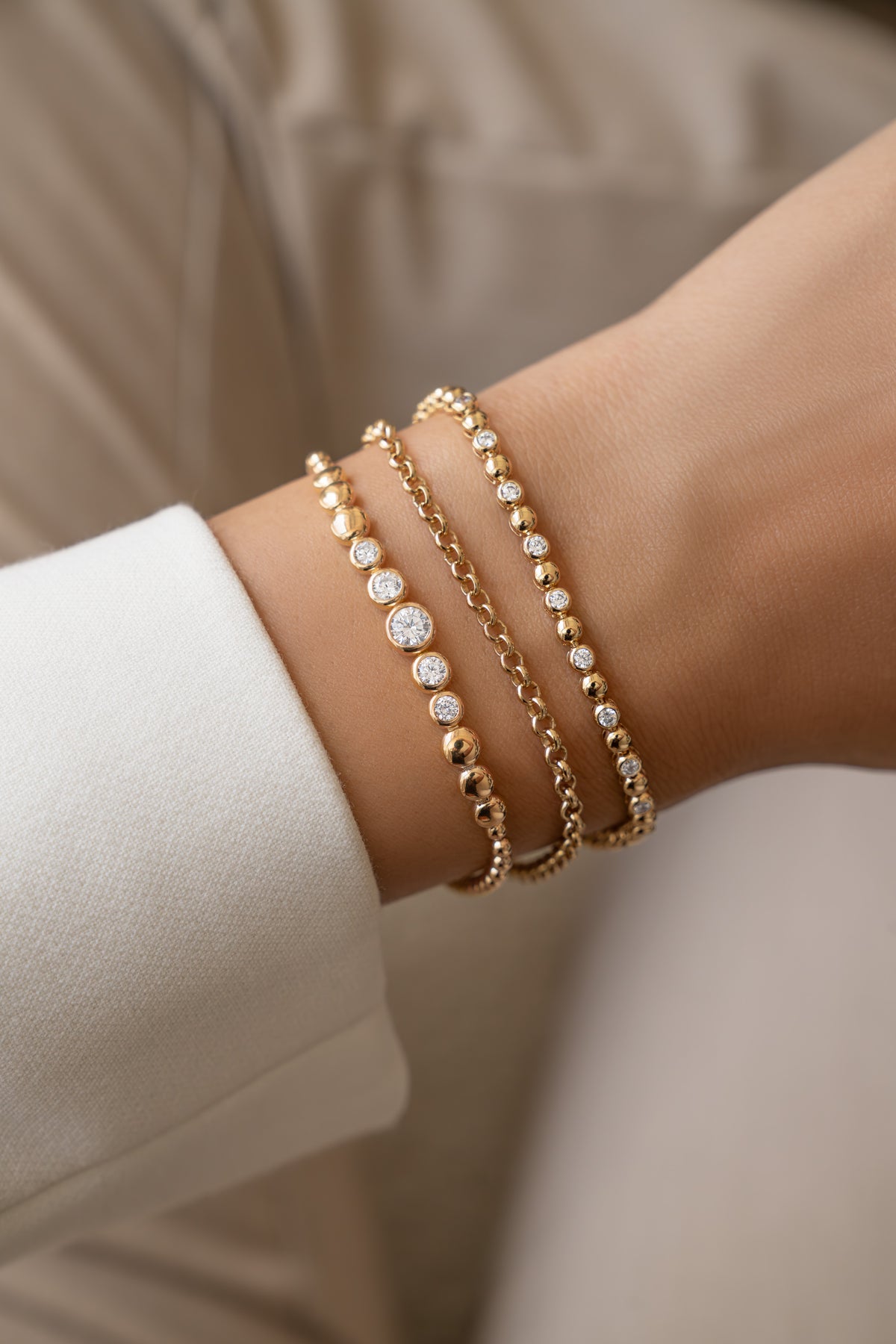 Gold graduated bezel tennis bracelet stacked with a rolo chain and bead-and-bezel bracelet on a wrist.