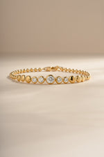 Gold graduated bezel tennis bracelet arranged on a cream background.