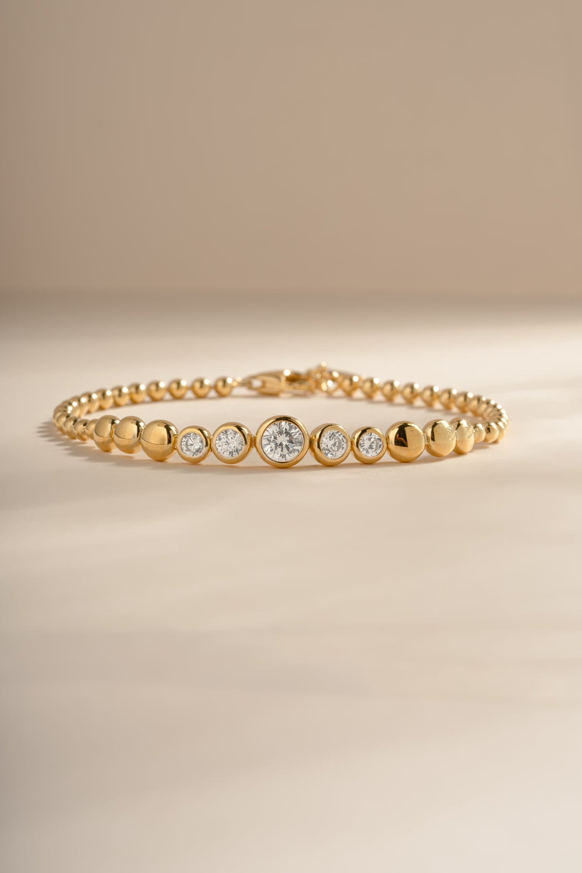 Gold graduated bezel tennis bracelet arranged on a cream background.