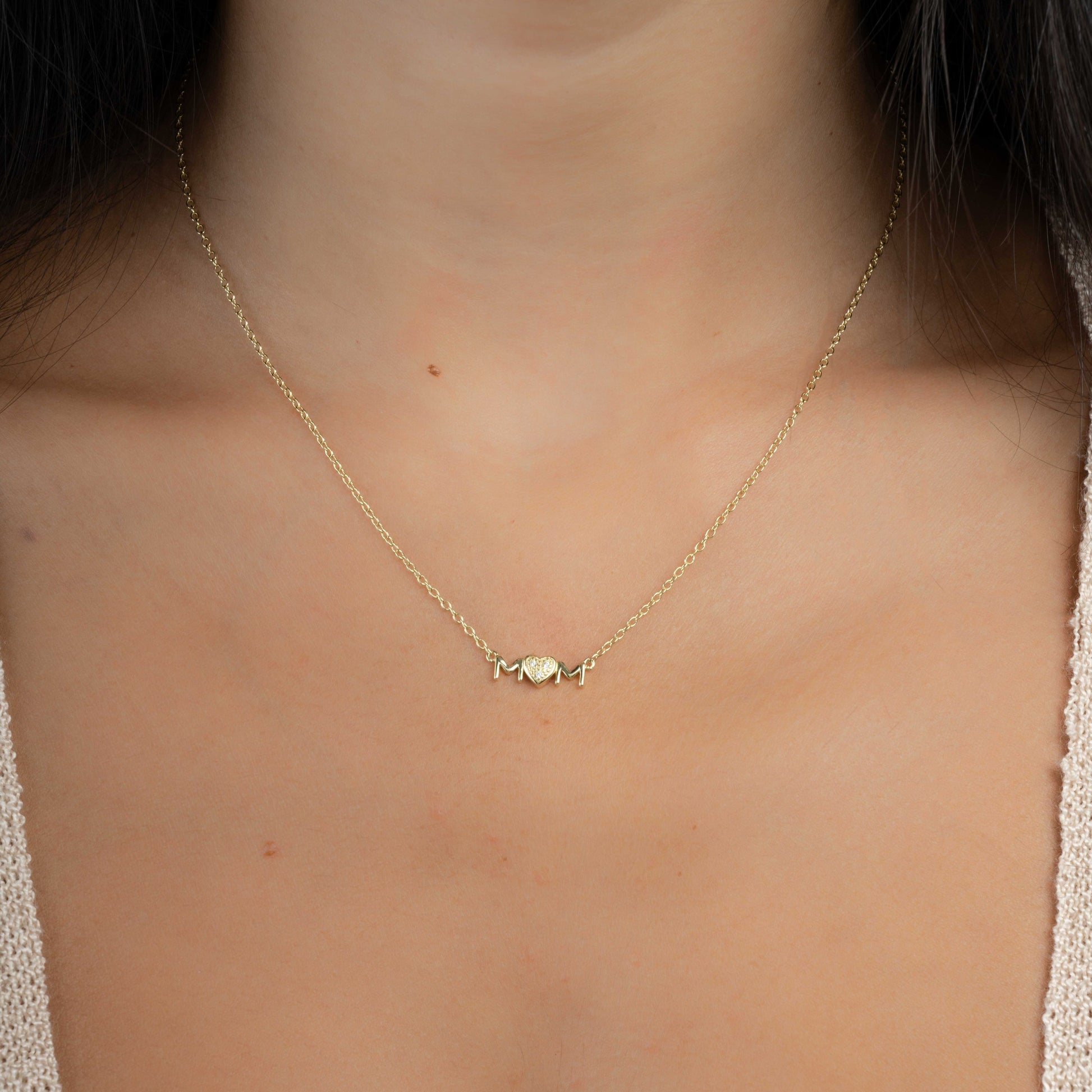 Model wearing a delicate pendant necklace that spells out "MOM" with CZ heart accent.