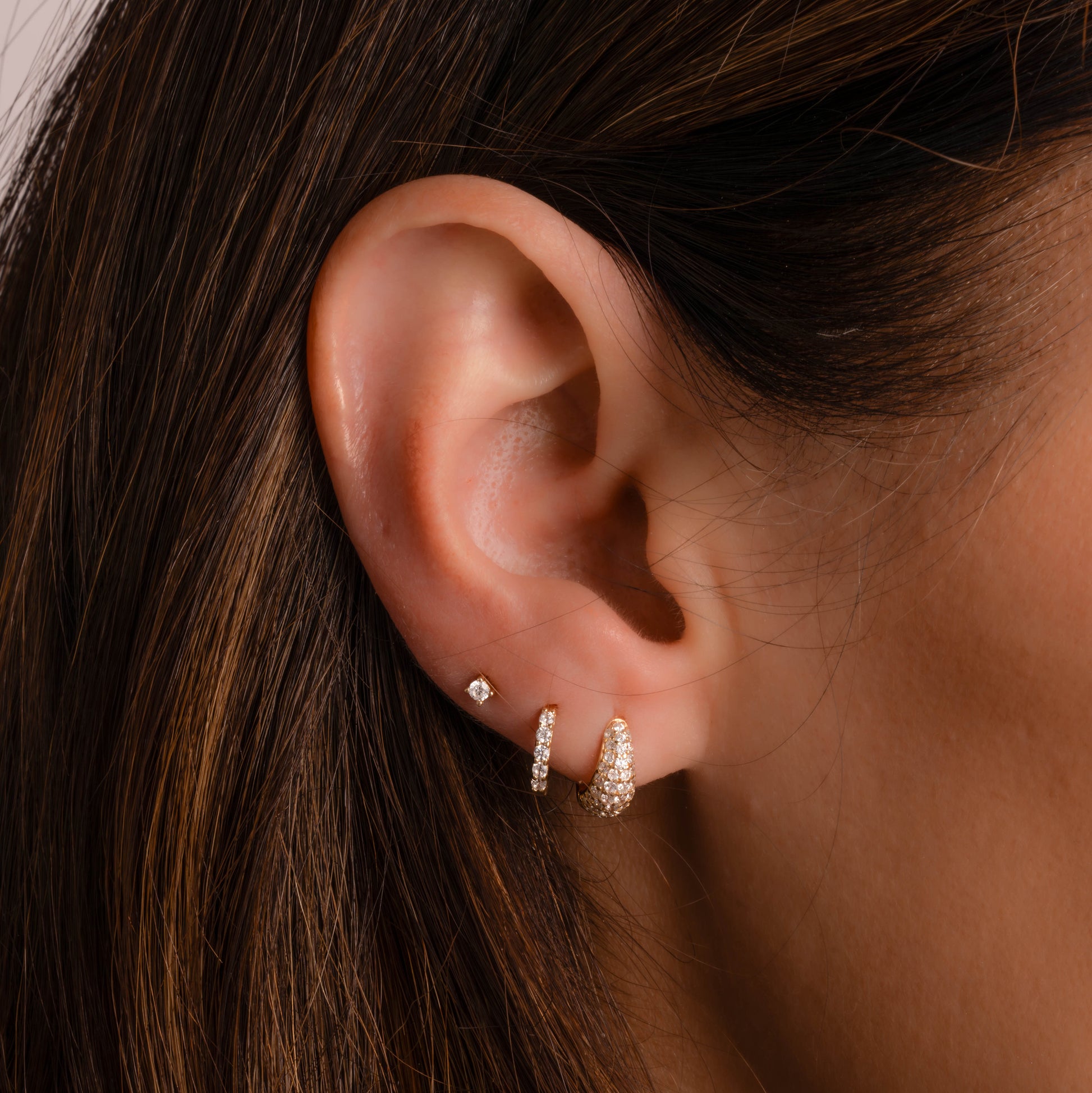 Model wearing gold hinged huggie hoop earrings with other pave diamond gold hoop earrings and diamond studs