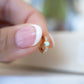 Close up image of fingers holding an opal and cz diamond studded huggie. The dainty opal earrings feature cz diamonds with a solitaire opal stone. 