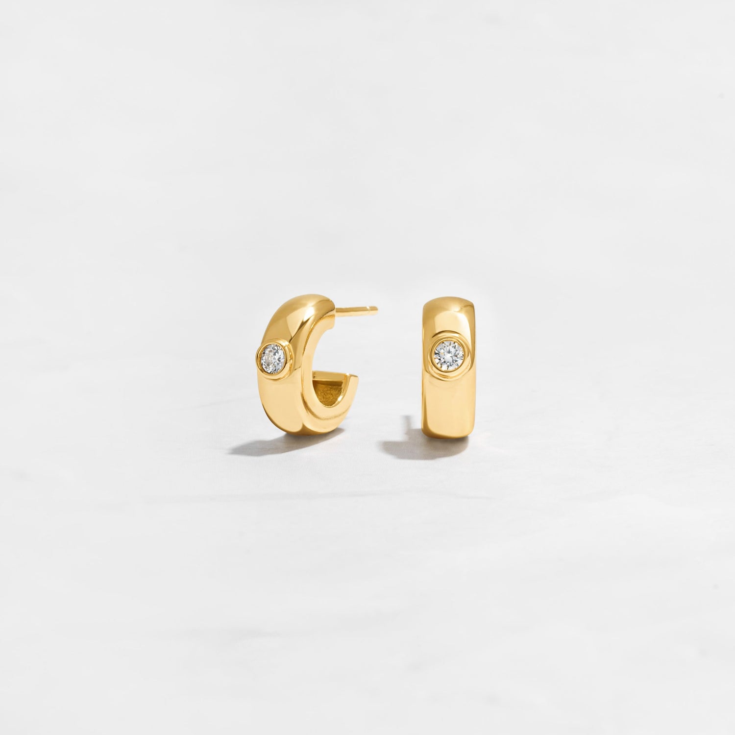 Closeup image of gold huggie hoops with diamond bezel design