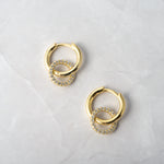 flay lay of gold hoop earrings and pavé charm, highlighting its fine details and shimmering diamonds. 