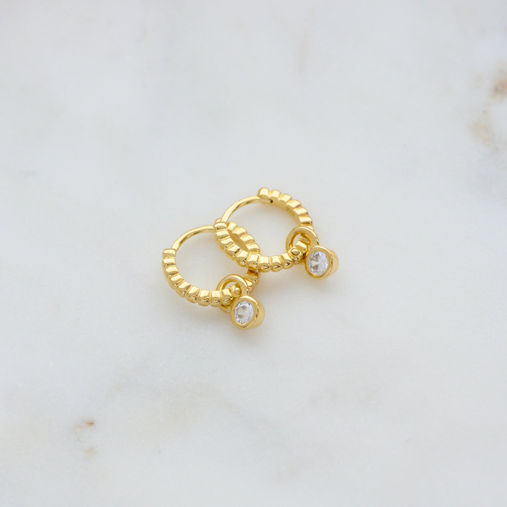 Gold beaded huggie hoops with bezel charm. 
