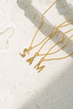gold initial necklace spelling out "Sam" neutral background