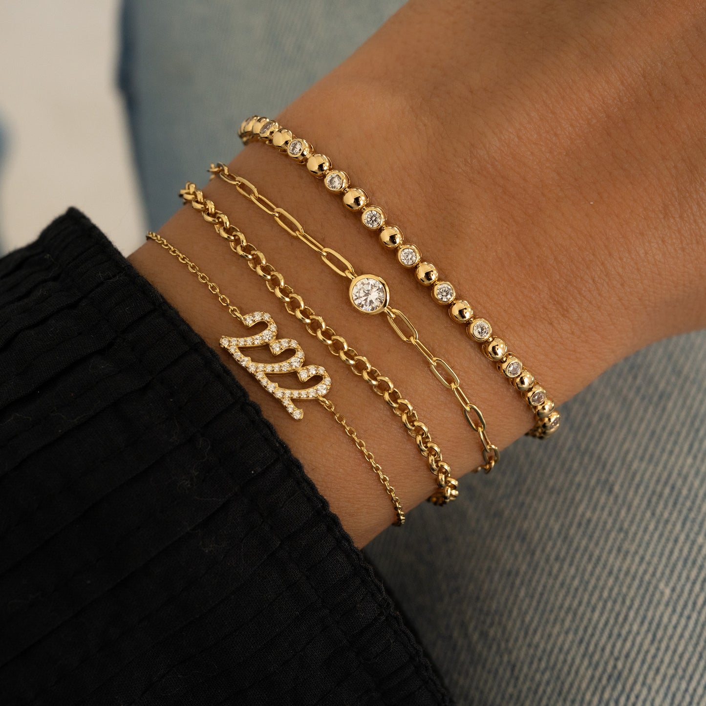 Gold link belcher chain bracelet stacked on model's wrist with other delicate gold chain bracelets and tennis bracelet. 