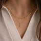model wearing a gold minimalist layering necklace featuring a charm paperclip necklace and a diamond shaped pendant with a round diamond center stone 