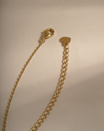 A gold-toned metal chain extender with a lobster clasp and a small heart-shaped tag, photographed on a plain light beige background.
