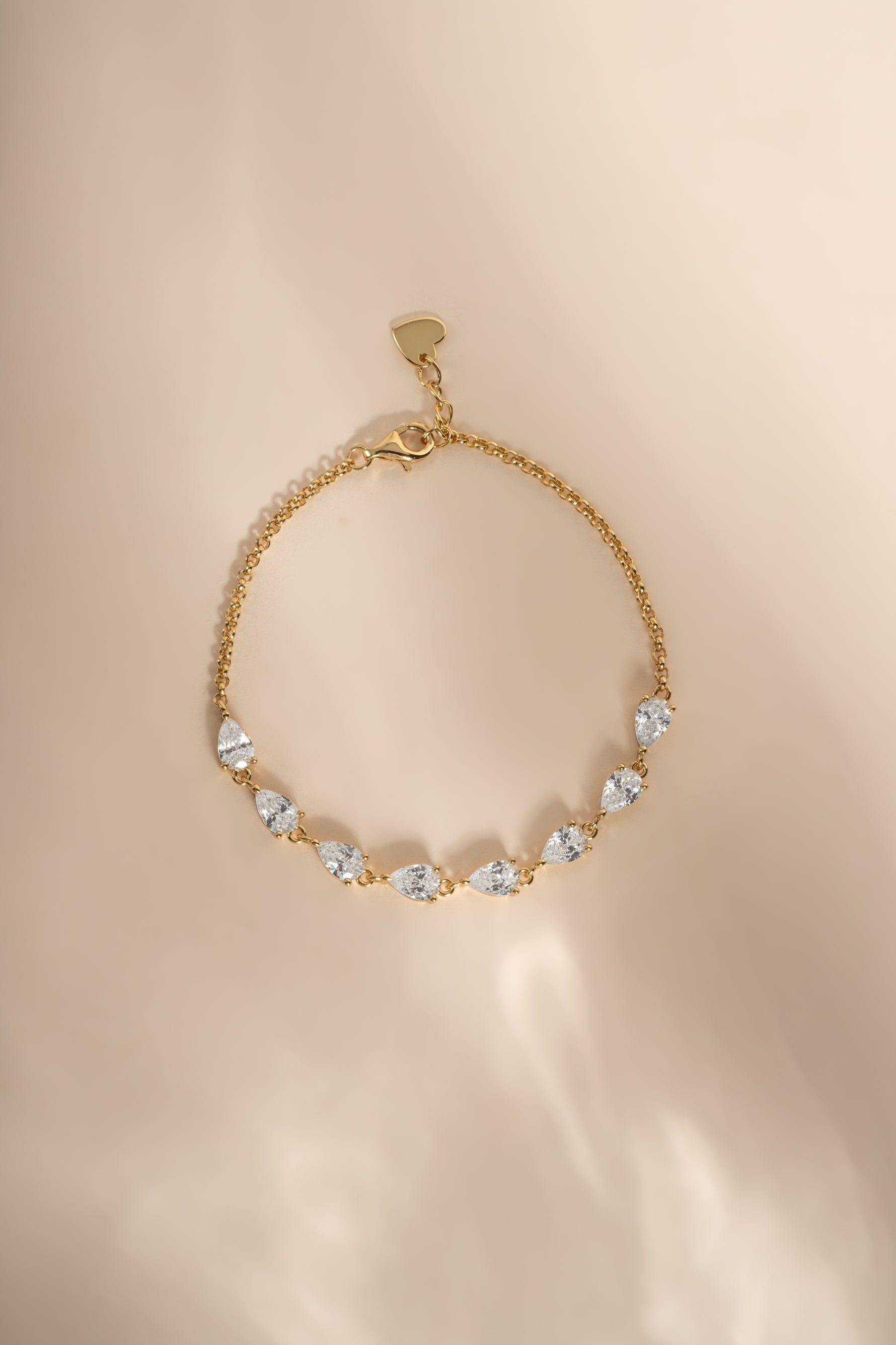 A delicate gold chain bracelet with a cascade of pear cut cubic zirconia stones on a chain bracelet set on a beige background