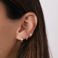 Close up image of model wearing three everyday minimalist opal earrings. The first piercing is a solitaire opal stone gold hoop earring, the second earring is a cz pave baby huggie, and the last earring is an opal baguette stud.