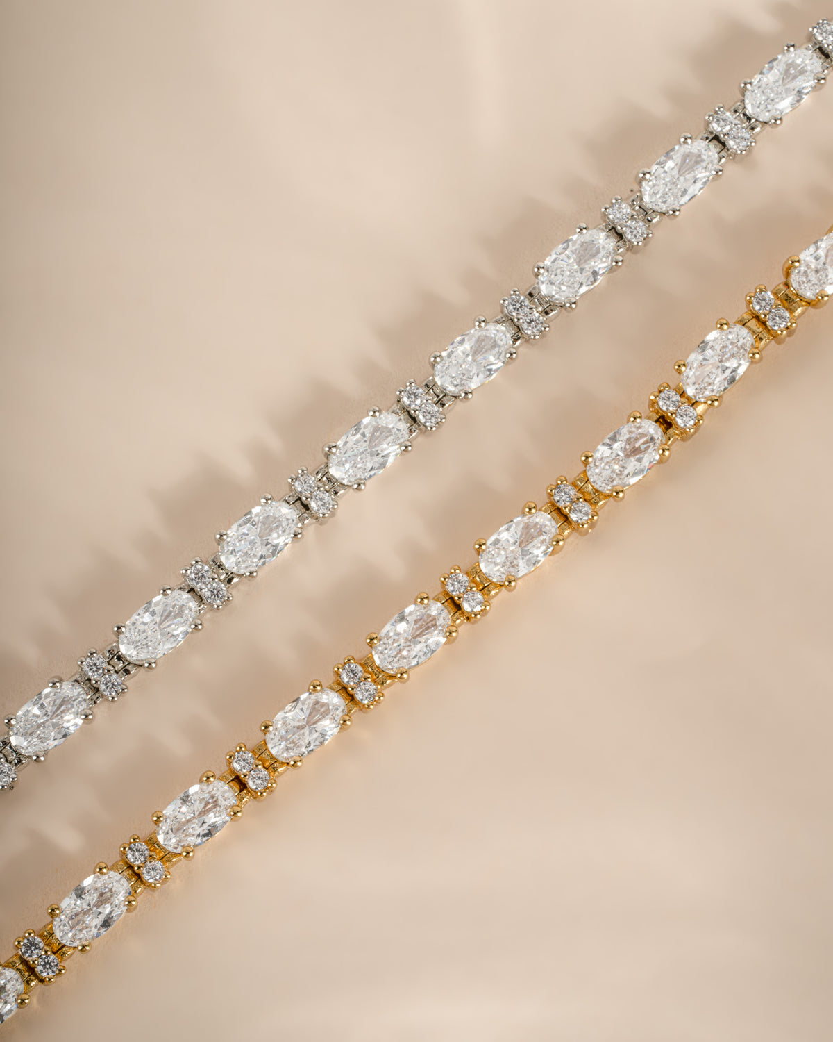 Two gold and silver tennis bracelets with each featuring oval and round white diamonds. 