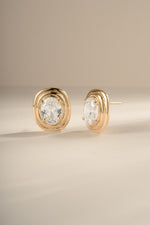Gold oval CZ statement studs showing the tiered setting and one post on a cream background.
