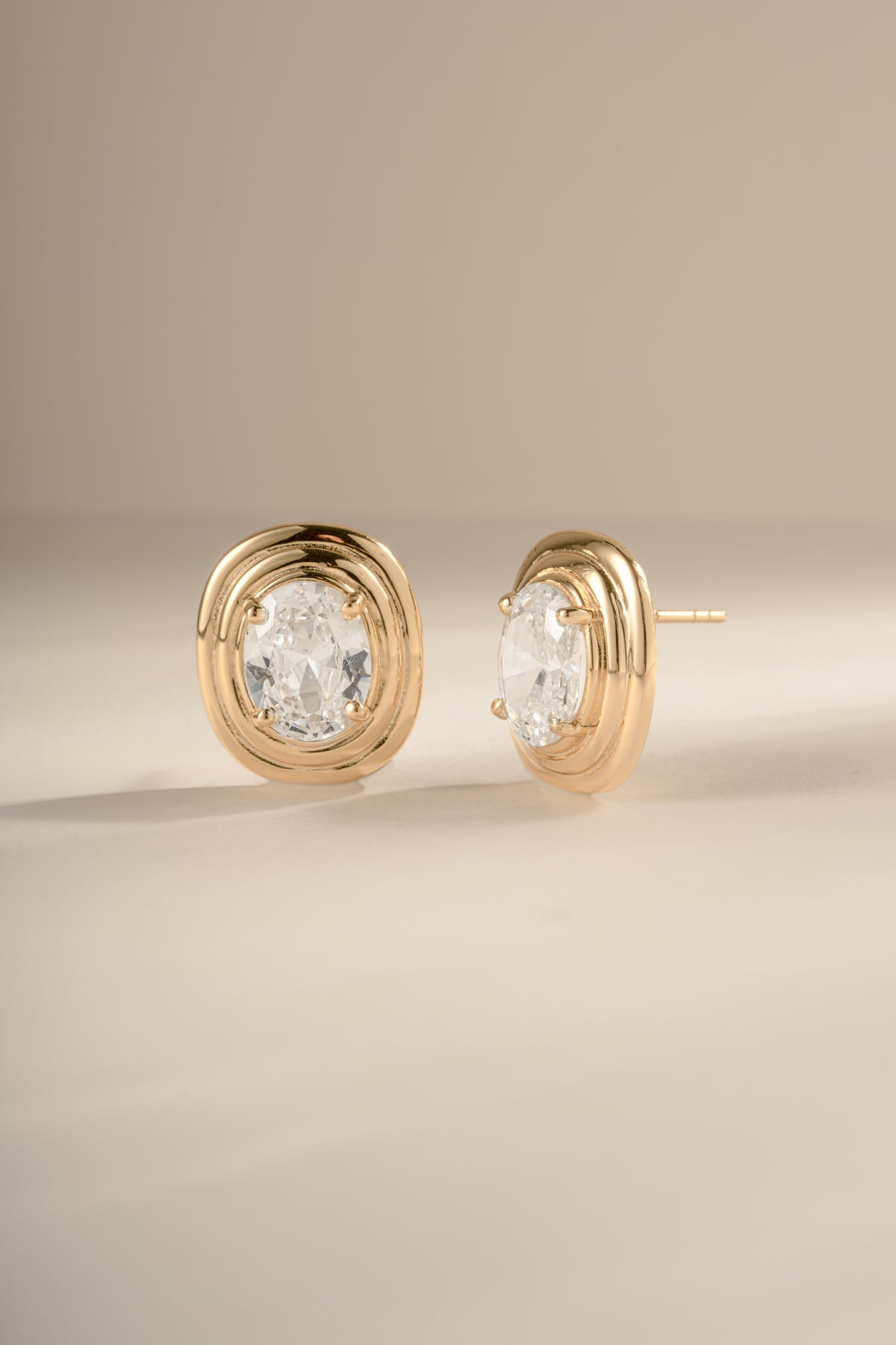Gold oval CZ statement studs showing the tiered setting and one post on a cream background.