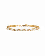 A gold tennis bracelet featuring white oval and round diamonds.