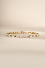 A gold tennis bracelet with oval and round clear stones.