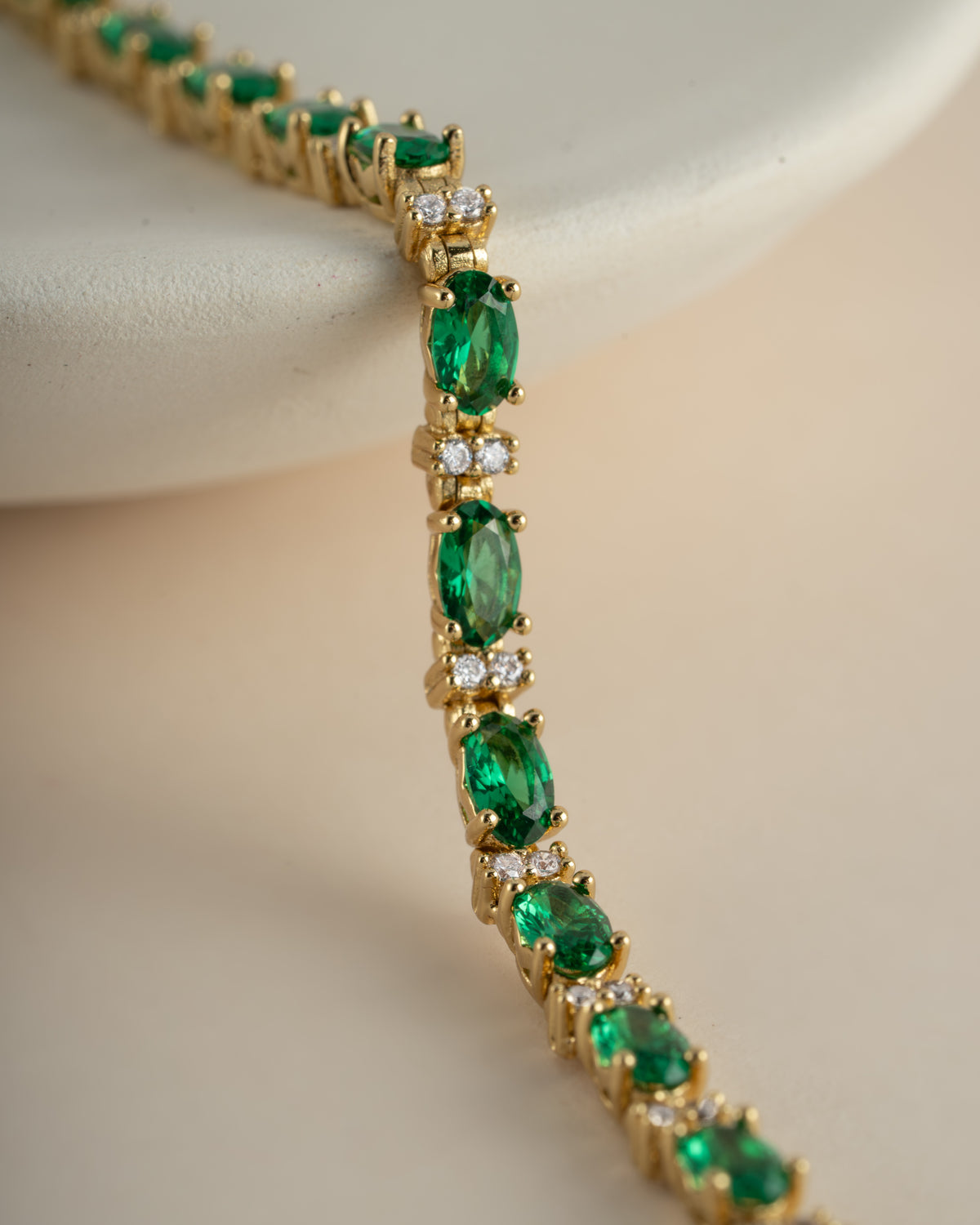Close-up of a gold tennis bracelet with oval-cut green stones and round white stones.