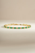 A gold tennis bracelet with round emerald and white cubic zirconia stones. 