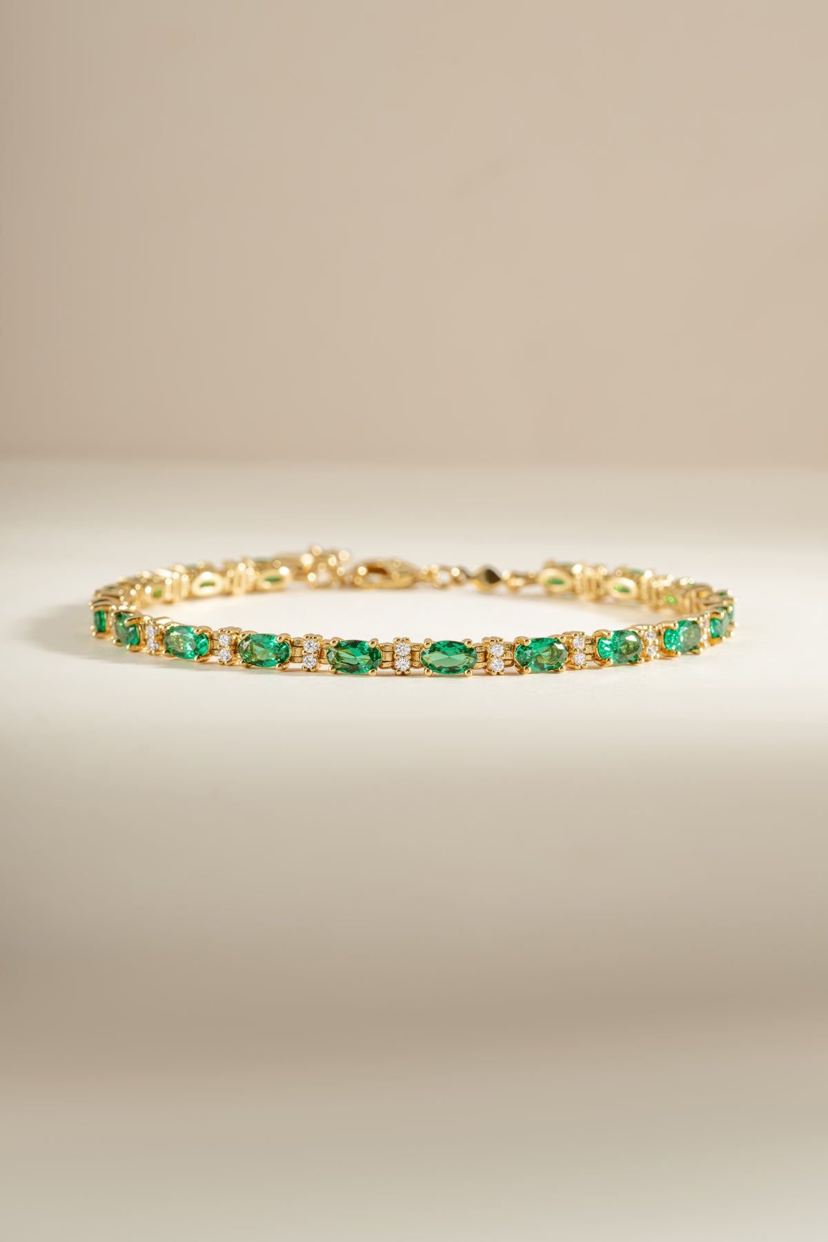 A gold tennis bracelet with round emerald and white cubic zirconia stones. 