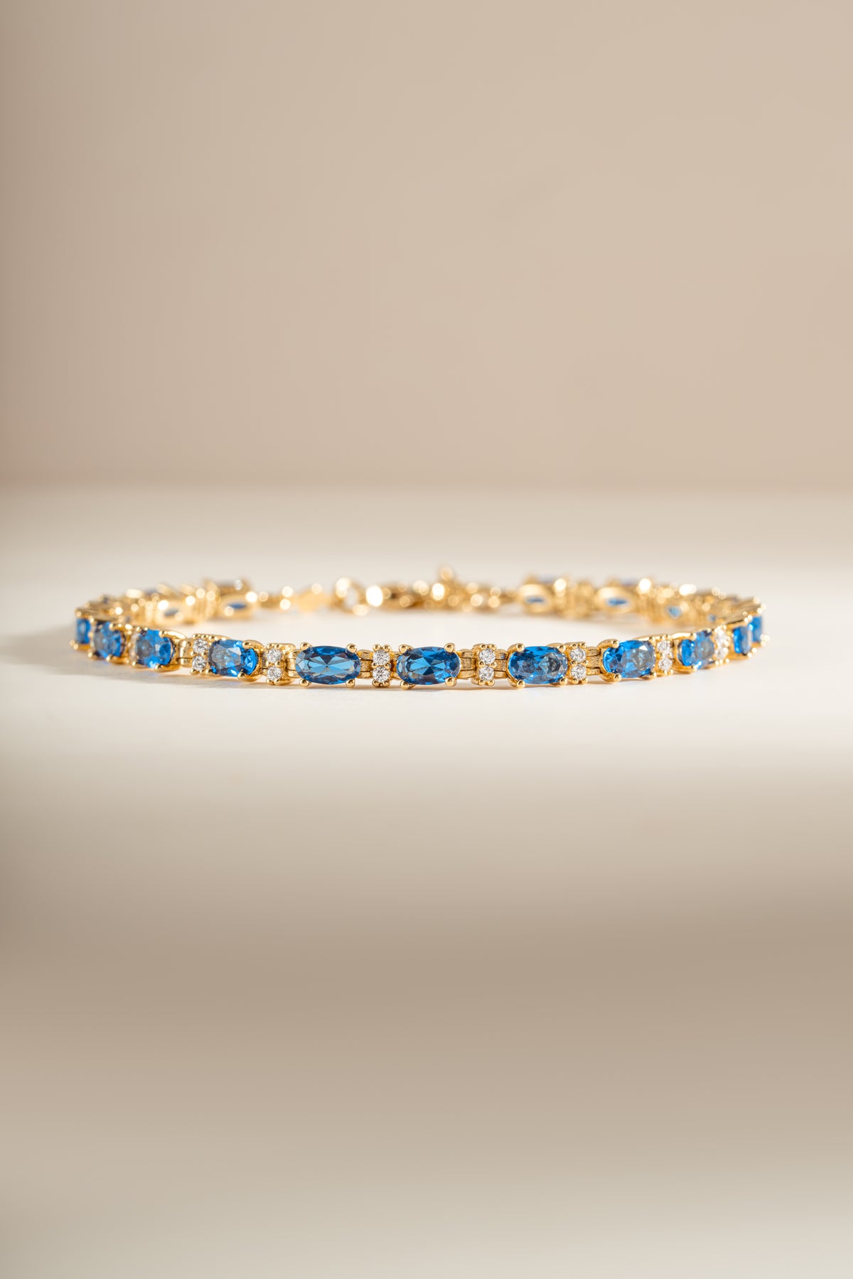 A gold tennis bracelet featuring oval-cut blue gemstones and alternating round diamonds.