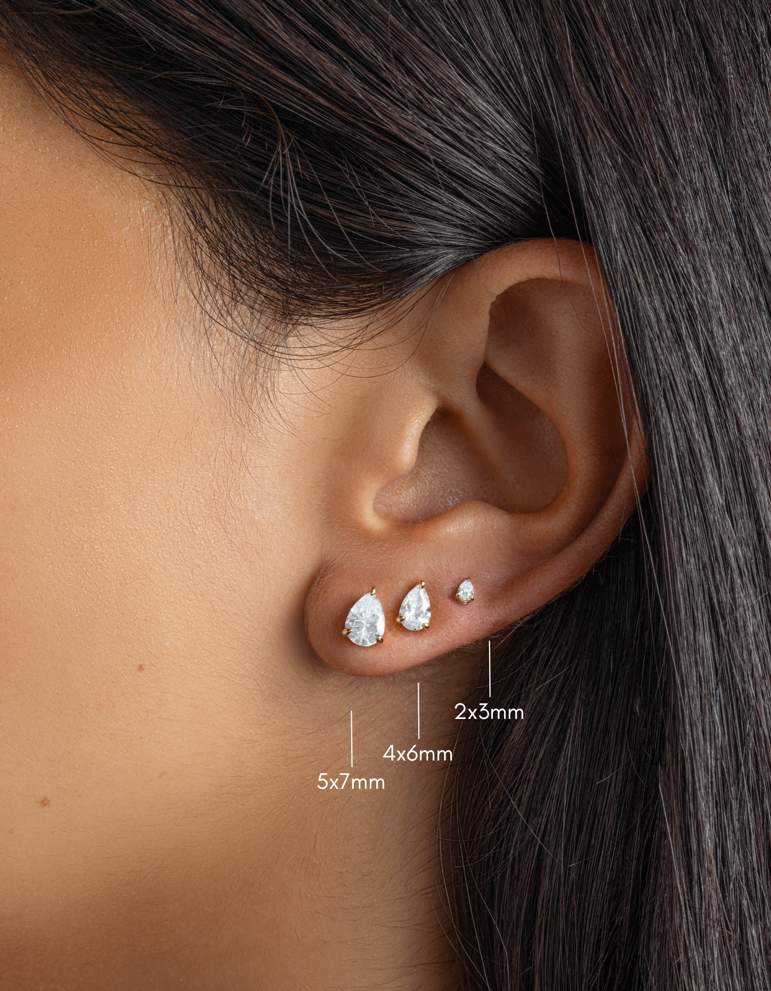 gold cubic zirconia stud earrings in various sizes, pear stud earring in 5x7mm, followed by a 4x6mm pear stud earring, and lastly, a 2x3mm pear stud earring on womens ear 