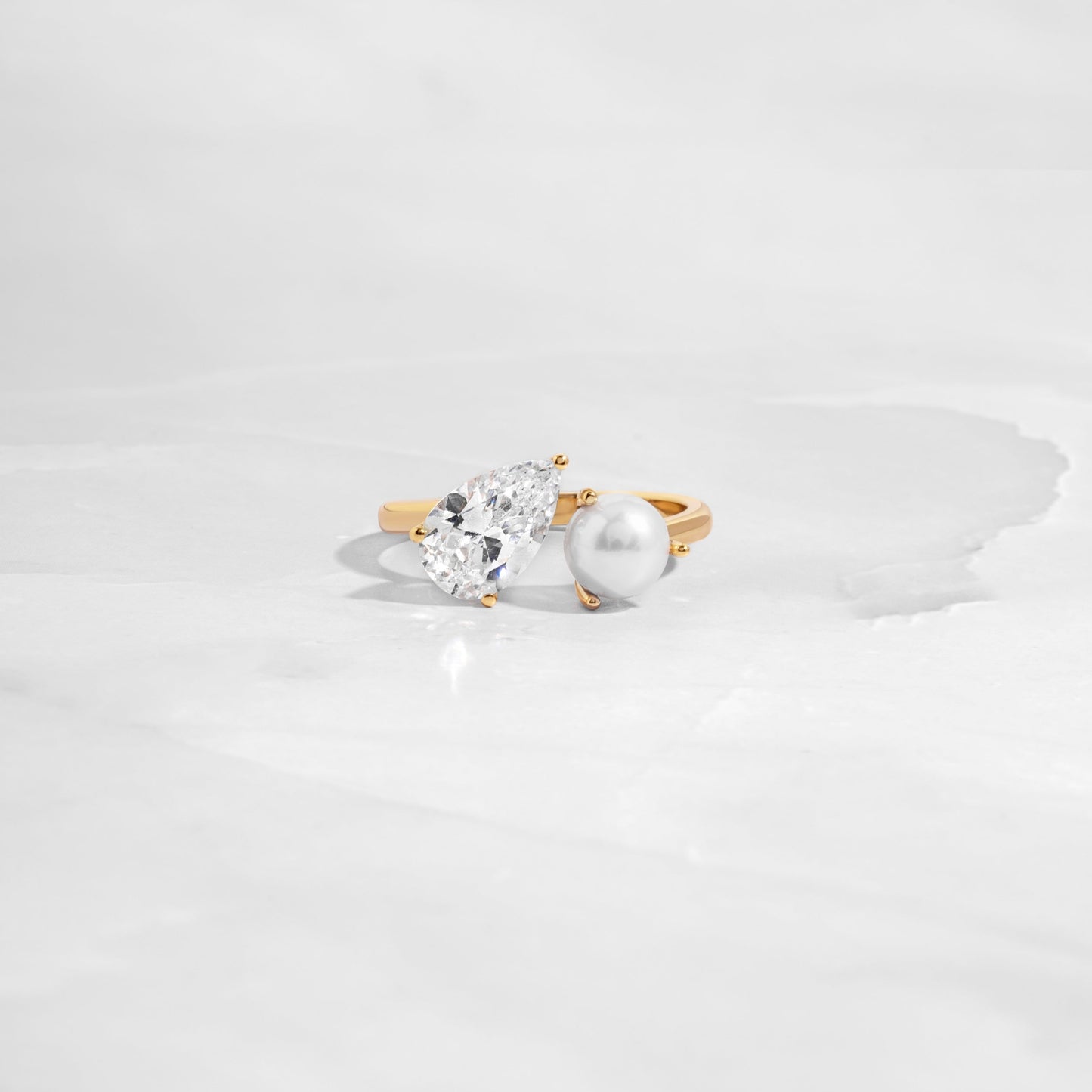 flat lay of toi et moi ring, with teardrop and freshwater pearl stone, set in sleek gold band as a statement ring. 