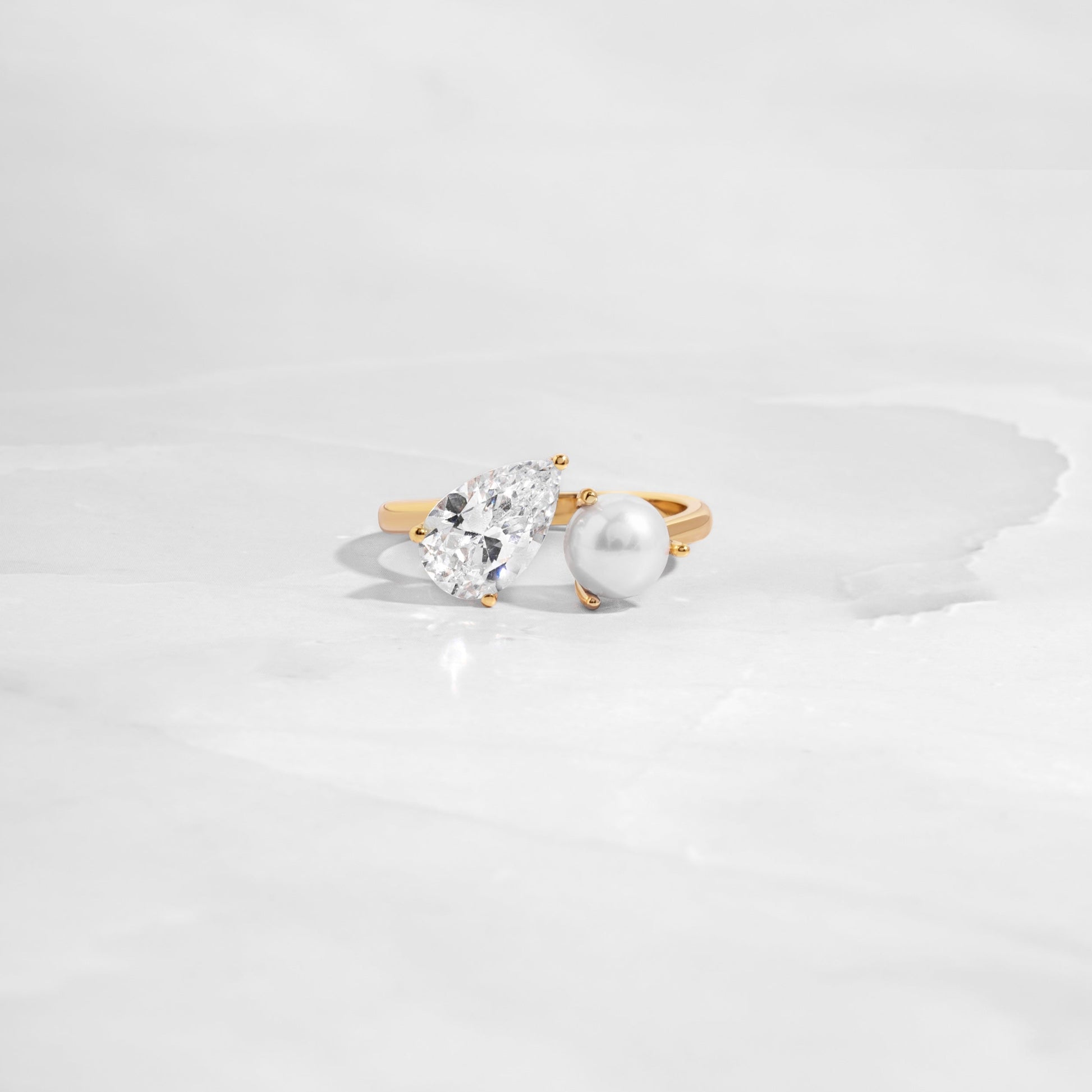 flat lay of toi et moi ring, with teardrop and freshwater pearl stone, set in sleek gold band as a statement ring. 