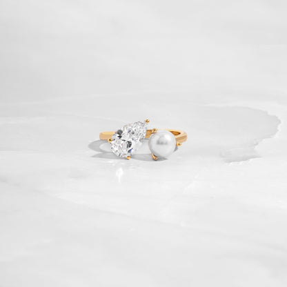 flat lay of toi et moi ring, with teardrop and freshwater pearl stone, set in sleek gold band as a statement ring. 