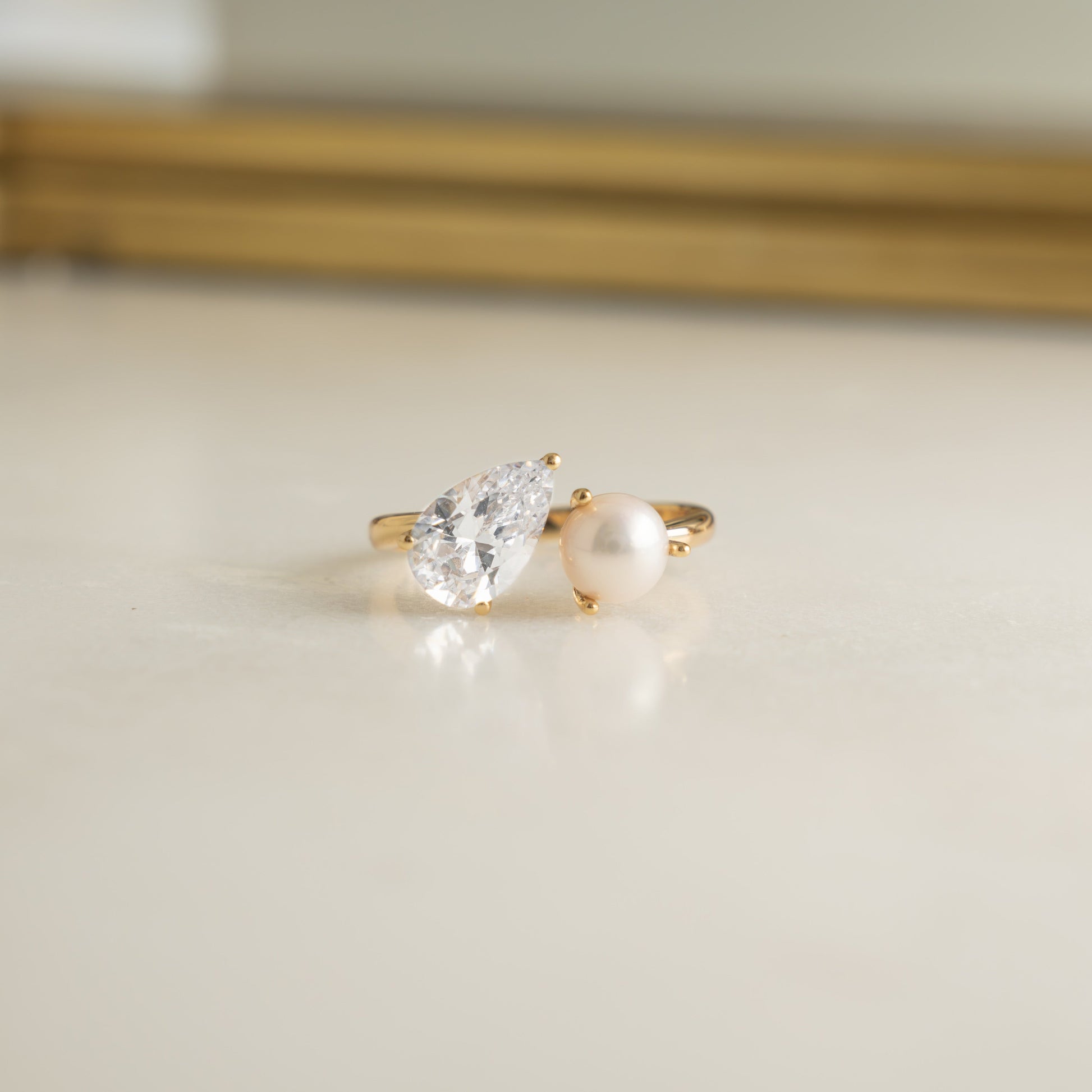 close up of Toi et Moi Ring, featuring a pear-shaped gemstone, with pearl, set in a sleek gold band