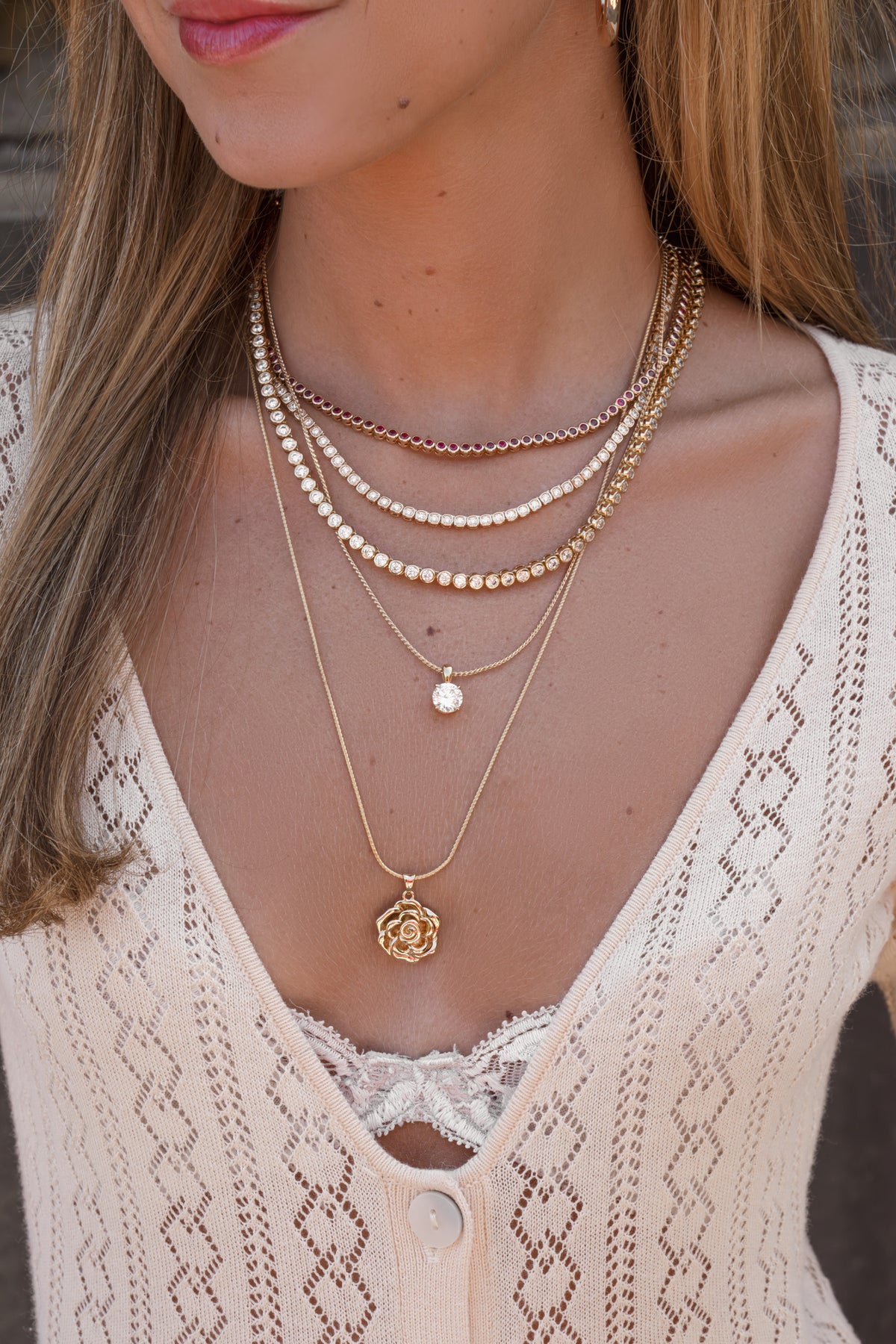 Ruby, square and round CZ bezel tennis necklaces in gold layered with a CZ solitaire pendant and a gold rose pendant necklace