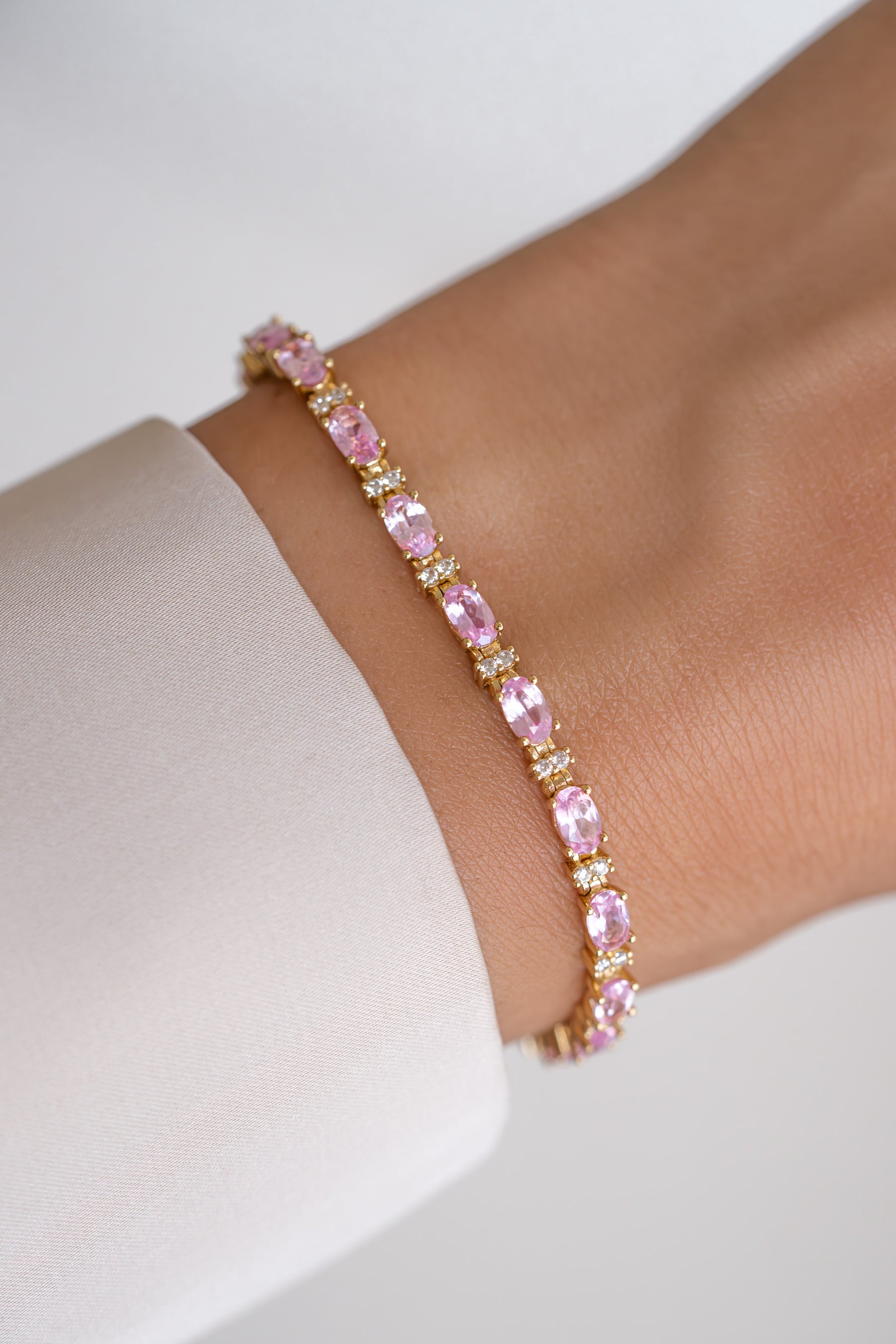 Closeup of a gold pink oval tennis bracelet with alternating round diamonds styled on model. 