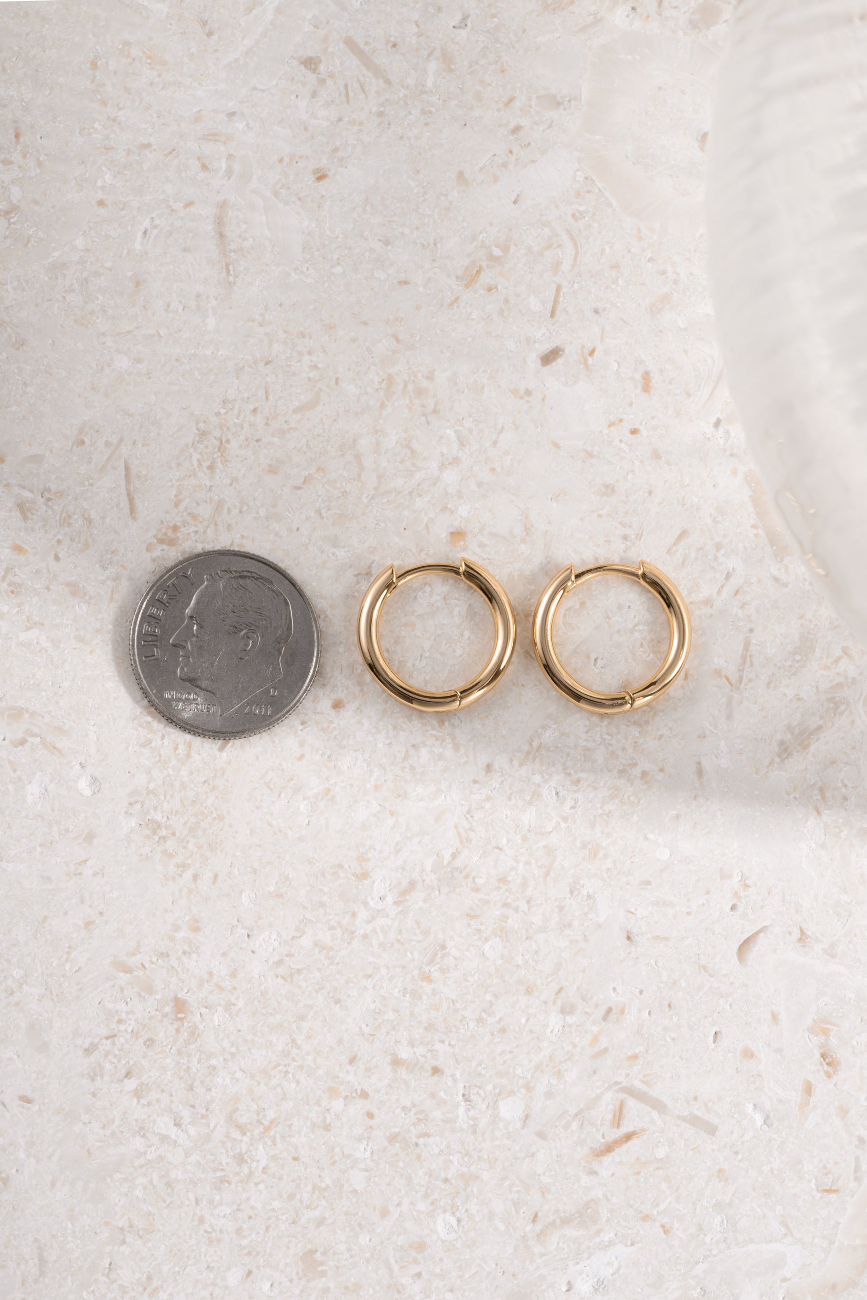 gold 11mm minimalist hoop earring being compared to size of dime neutral background