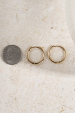 gold 13mm minimalist hoop earrings on a neutral background being compared to the  size of a dime