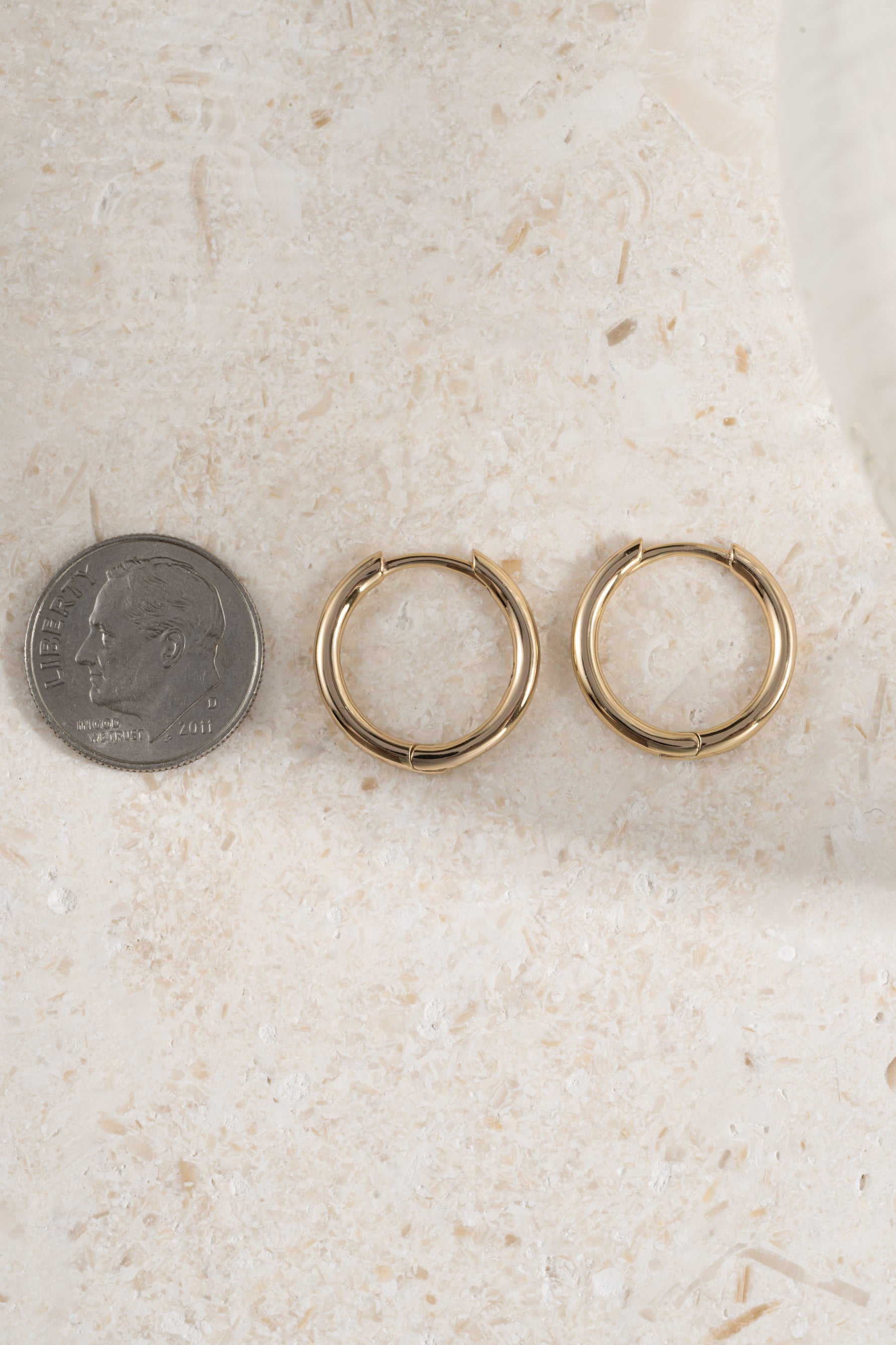 gold 13mm minimalist hoop earrings on a neutral background being compared to the  size of a dime