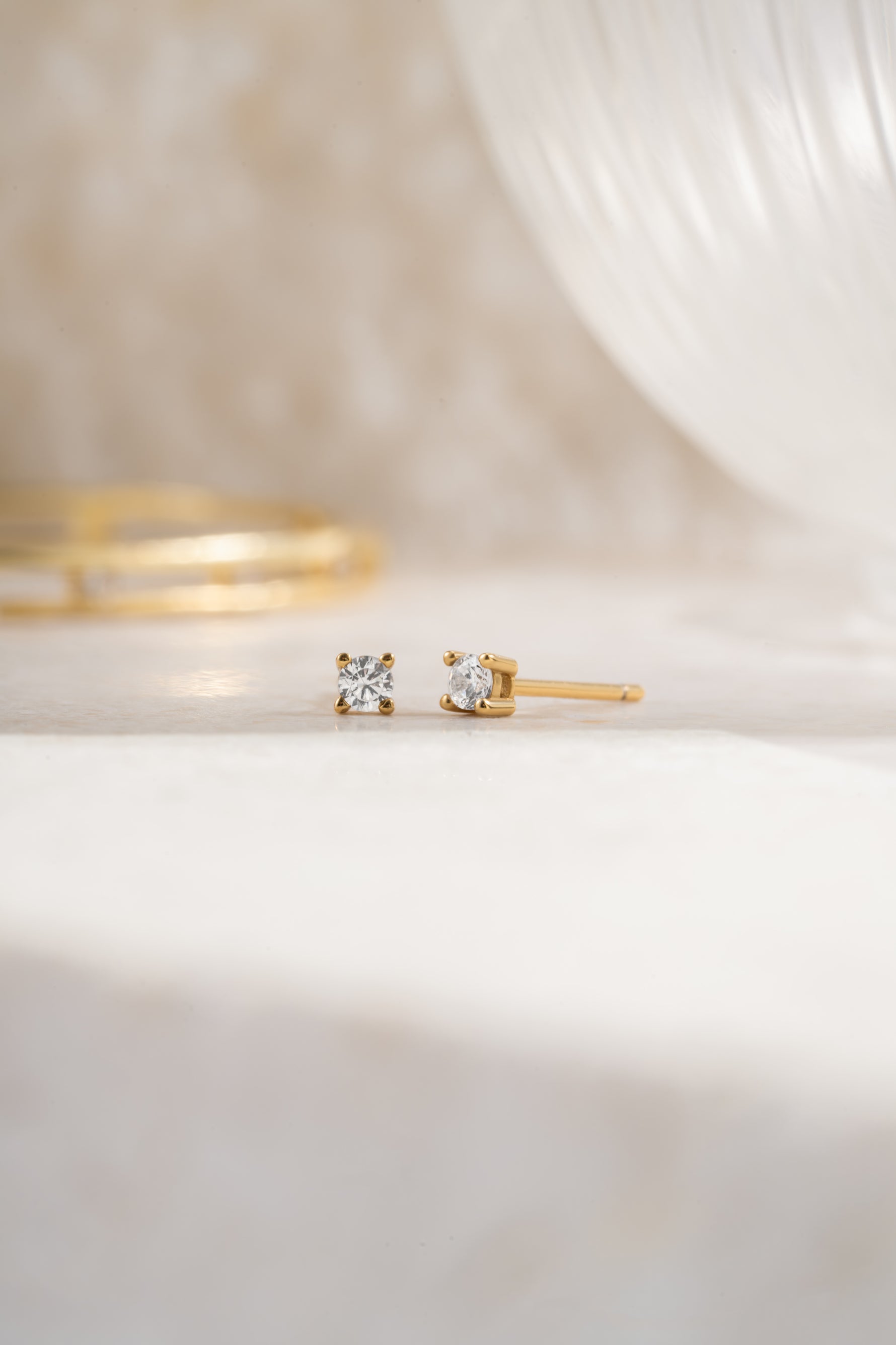 Gold 2.5mm diamond solitaire stud earring on angle plain background