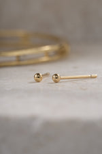 gold 2mm ball stud earring on a neutral background