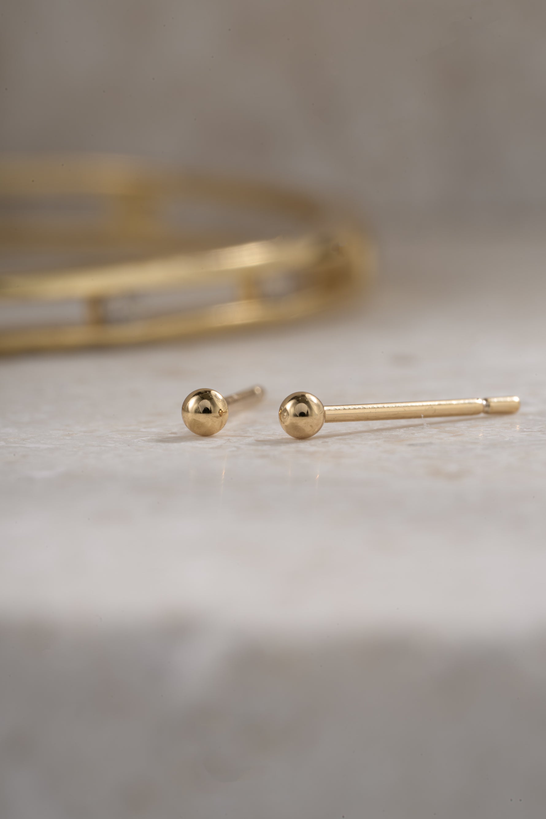 gold 2mm ball stud earring on a neutral background
