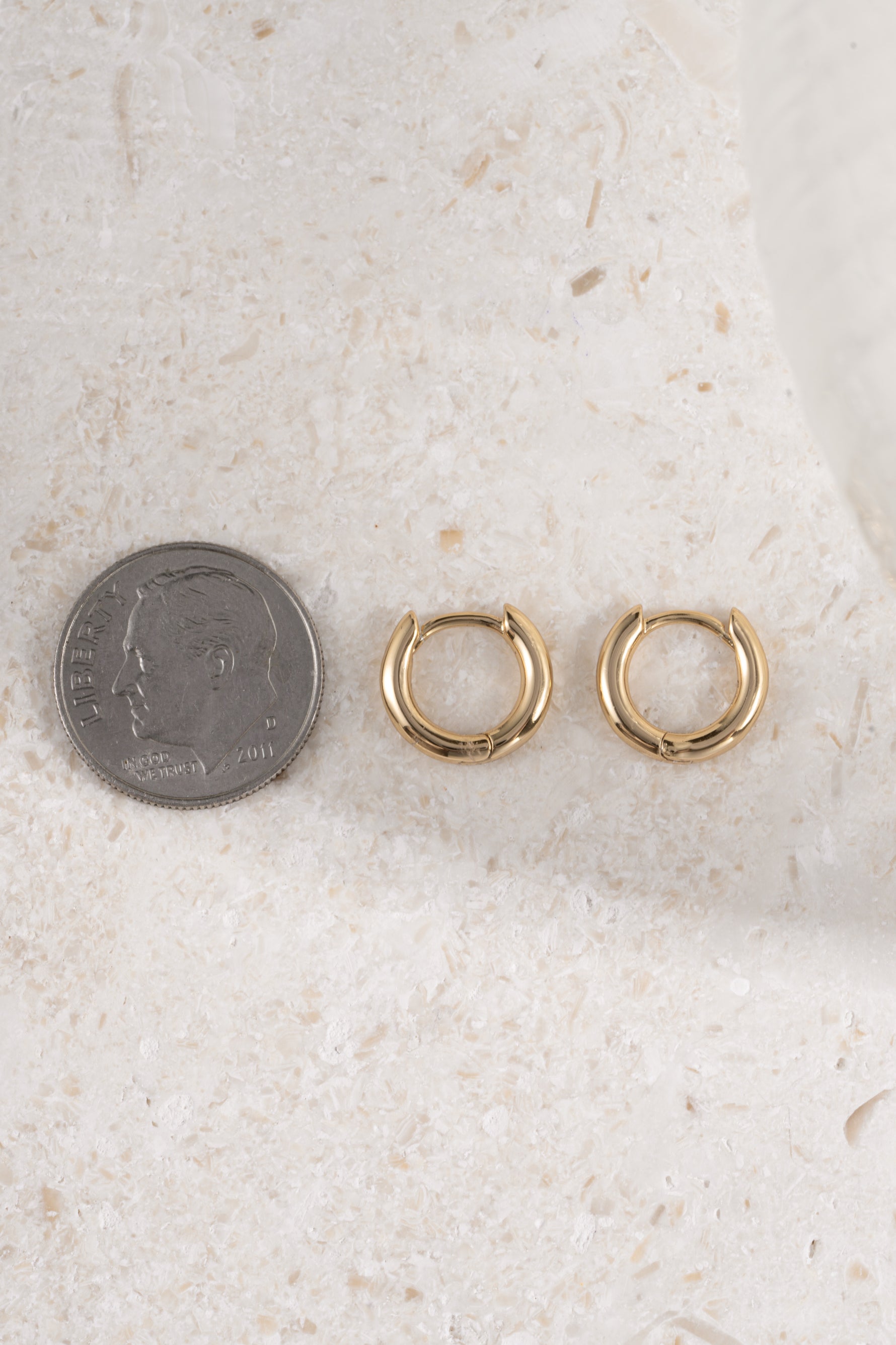 8mm gold hoop earring being compare to size of dime on neutral background