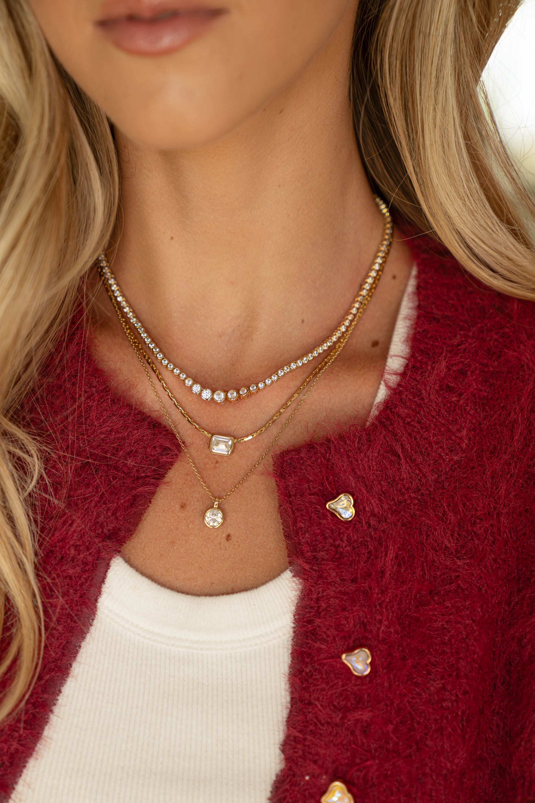 Gold baguette necklace layered with other gold necklaces on women wearing red sweater