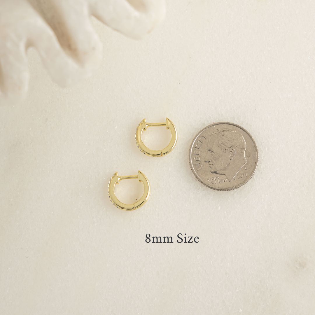 Gold hoop earrings next to a quarter on a beige background